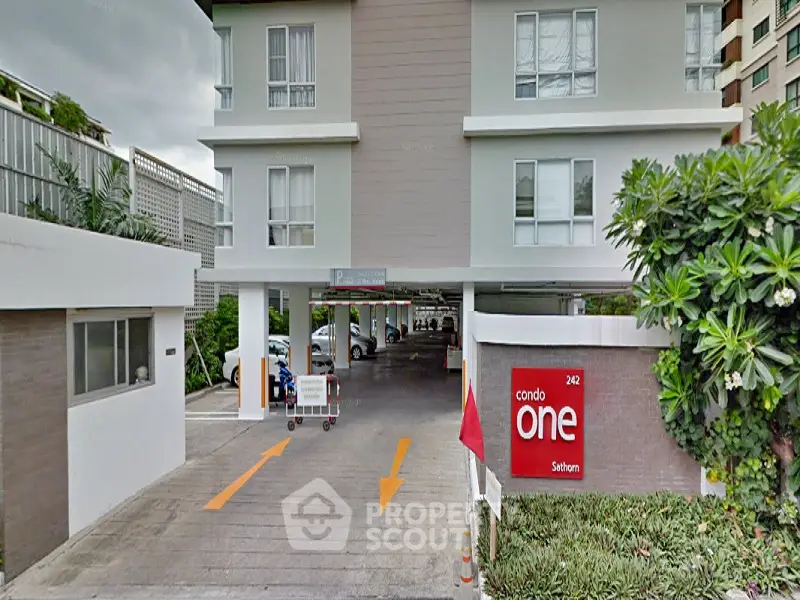 Modern condo entrance with parking area and lush greenery.