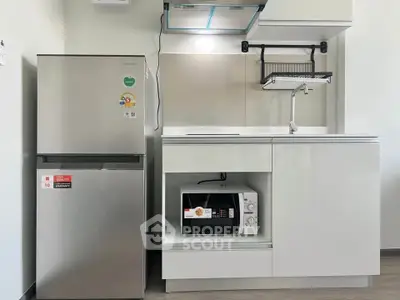 Modern kitchen with sleek white cabinets, stainless steel fridge, and built-in microwave.