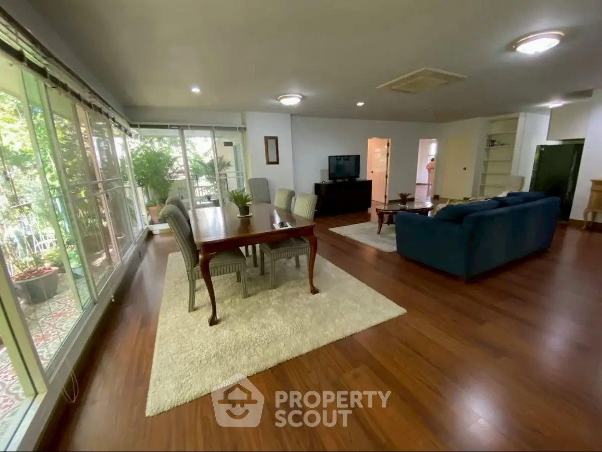 Spacious living room with elegant dining area and large windows overlooking greenery.