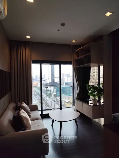 Modern living room with city view, featuring stylish furniture and large windows for natural light.