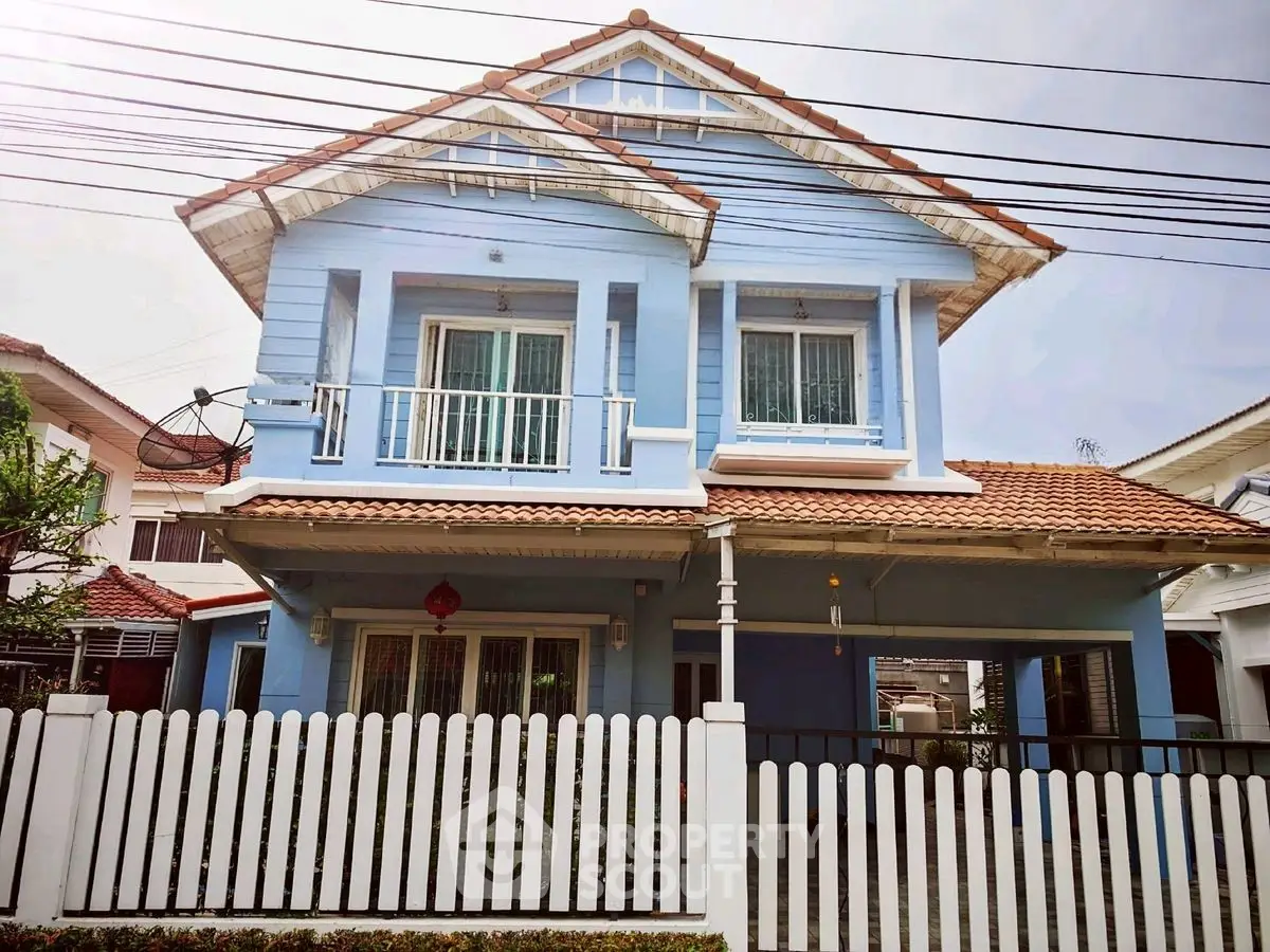 Charming blue two-story house with white picket fence and tiled roof in suburban neighborhood.