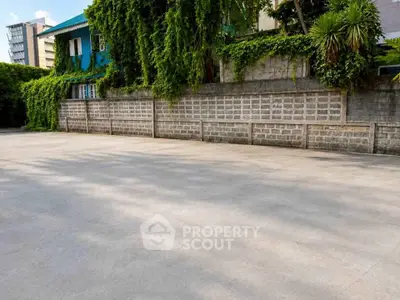 Spacious outdoor parking area with lush greenery and brick wall backdrop.