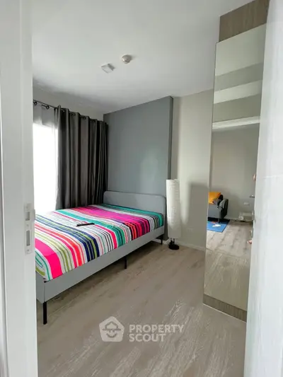 Modern bedroom with colorful striped bedding and large mirror, featuring natural light and sleek flooring.