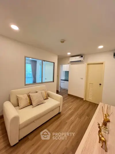 Modern living room with cozy sofa and wooden flooring, leading to a bright kitchen area.