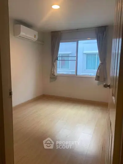 Cozy empty bedroom with wooden flooring and air conditioning, ready for personal touch.