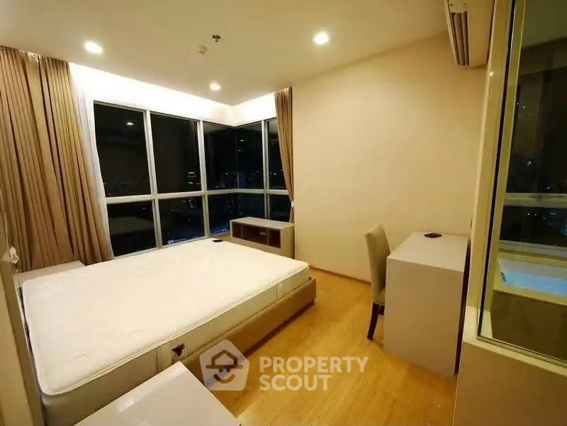 Spacious bedroom with large windows and modern furnishings in a high-rise apartment.