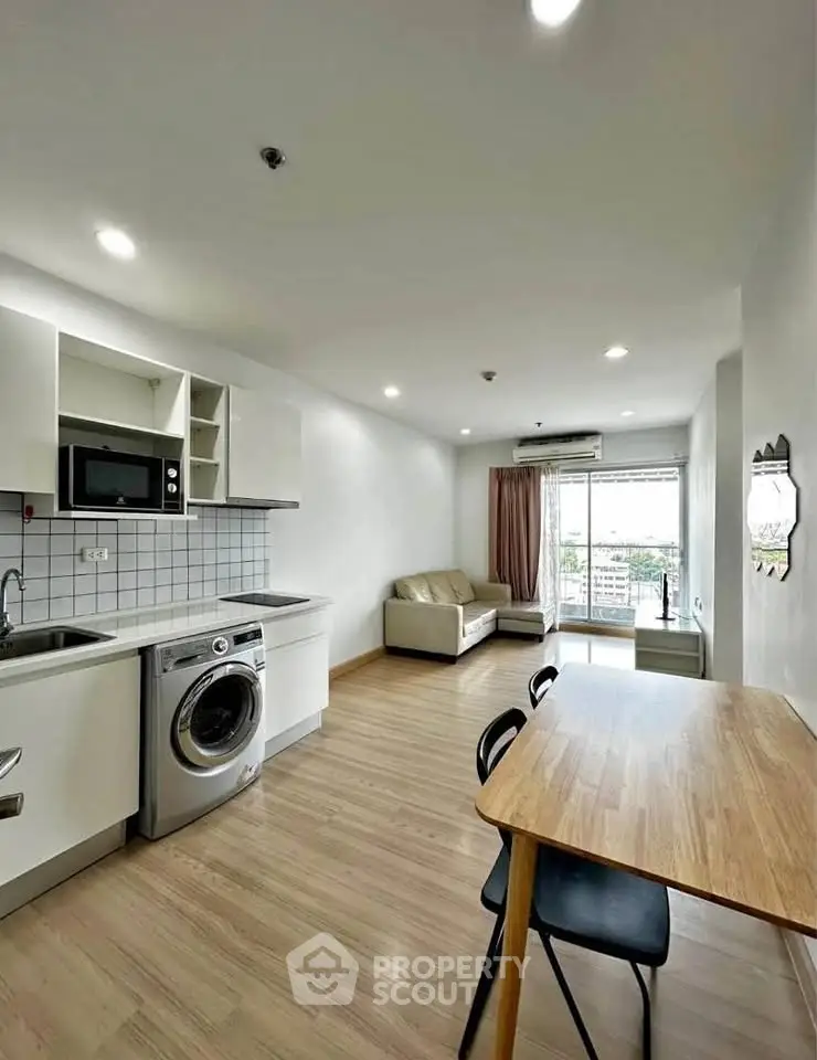 Modern open-plan living room with kitchen, featuring washing machine and balcony view.