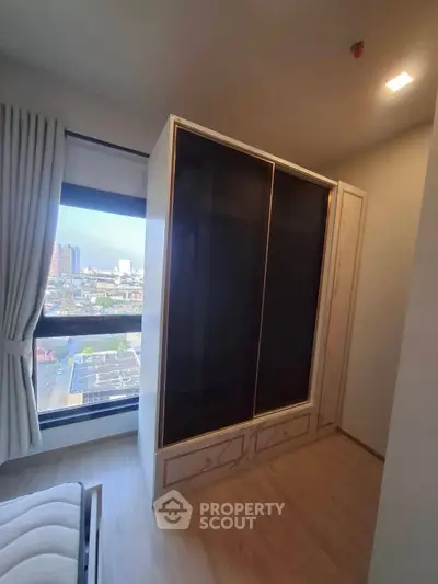 Modern bedroom with large window and built-in wardrobe offering city views.