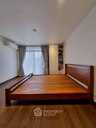 Spacious bedroom with wooden flooring and large window for natural light.