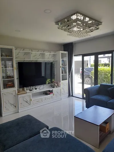 Elegant living room with modern chandelier and large TV, featuring stylish marble cabinetry and plush blue seating.