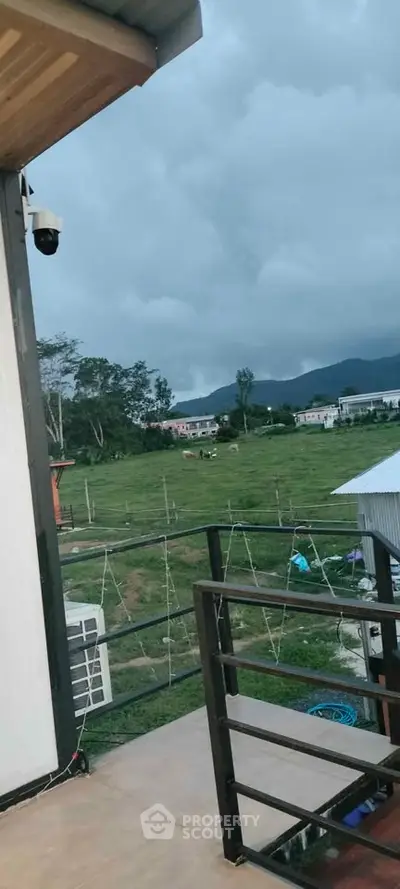 Scenic balcony view overlooking lush green fields and distant mountains.