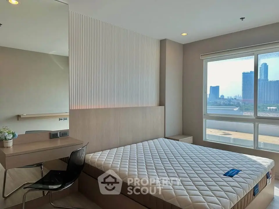 Modern bedroom with city view, featuring a sleek desk and large window for natural light.