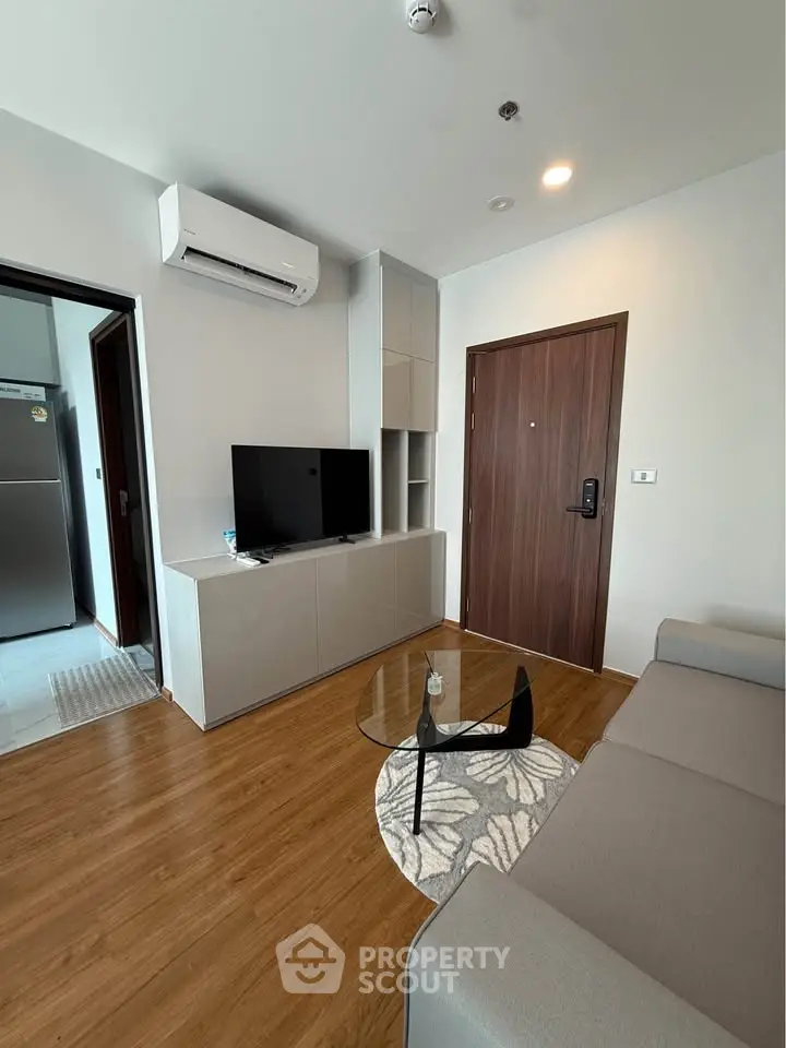Modern living room with sleek furniture and wooden flooring, featuring a TV and air conditioning.