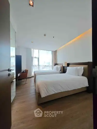 Spacious modern bedroom with twin beds and large windows offering natural light.