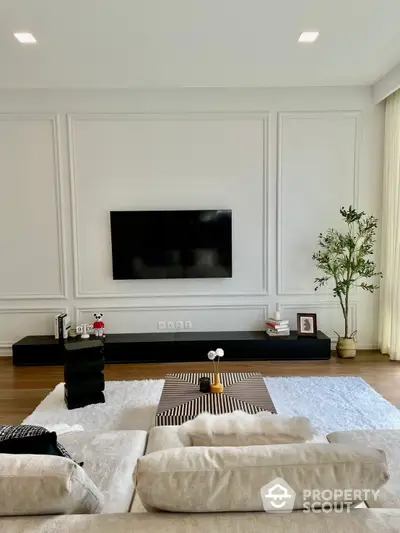 Elegant living room with high ceilings, classic wall panels, and a modern entertainment unit, complemented by a lush indoor plant and plush seating area.