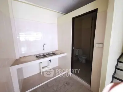 Compact kitchen area with dual sink and adjacent bathroom in a minimalist design.
