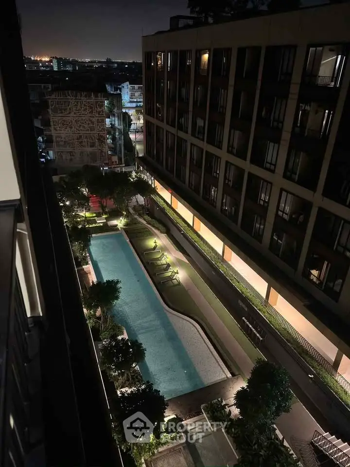 Stunning night view of a modern apartment complex with illuminated pool and lush greenery.