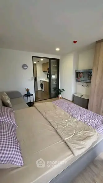Modern bedroom with cozy bedding and view into a stylish kitchen area, perfect for urban living.