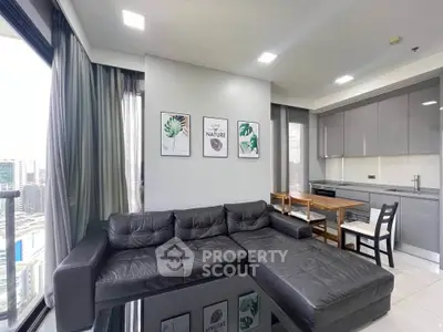 Modern living room with sleek black leather sofa and open kitchen layout in a high-rise apartment.