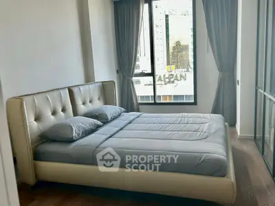 Modern bedroom with large window and city view, featuring a stylish bed and elegant curtains.