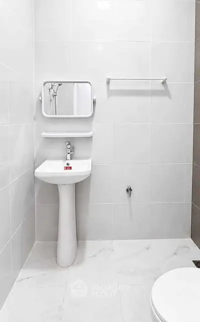 Minimalist bathroom with white pedestal sink and wall-mounted mirror in modern apartment.