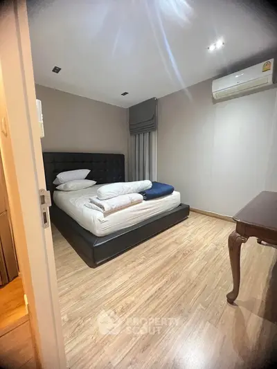 Cozy bedroom with modern decor and wooden flooring, featuring a comfortable bed and air conditioning.