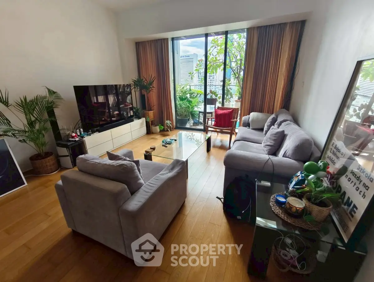 Spacious living room with large windows and city view, featuring modern furniture and wooden flooring.