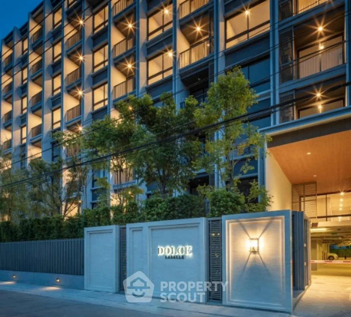 Modern condominium building exterior with illuminated facade and lush greenery.