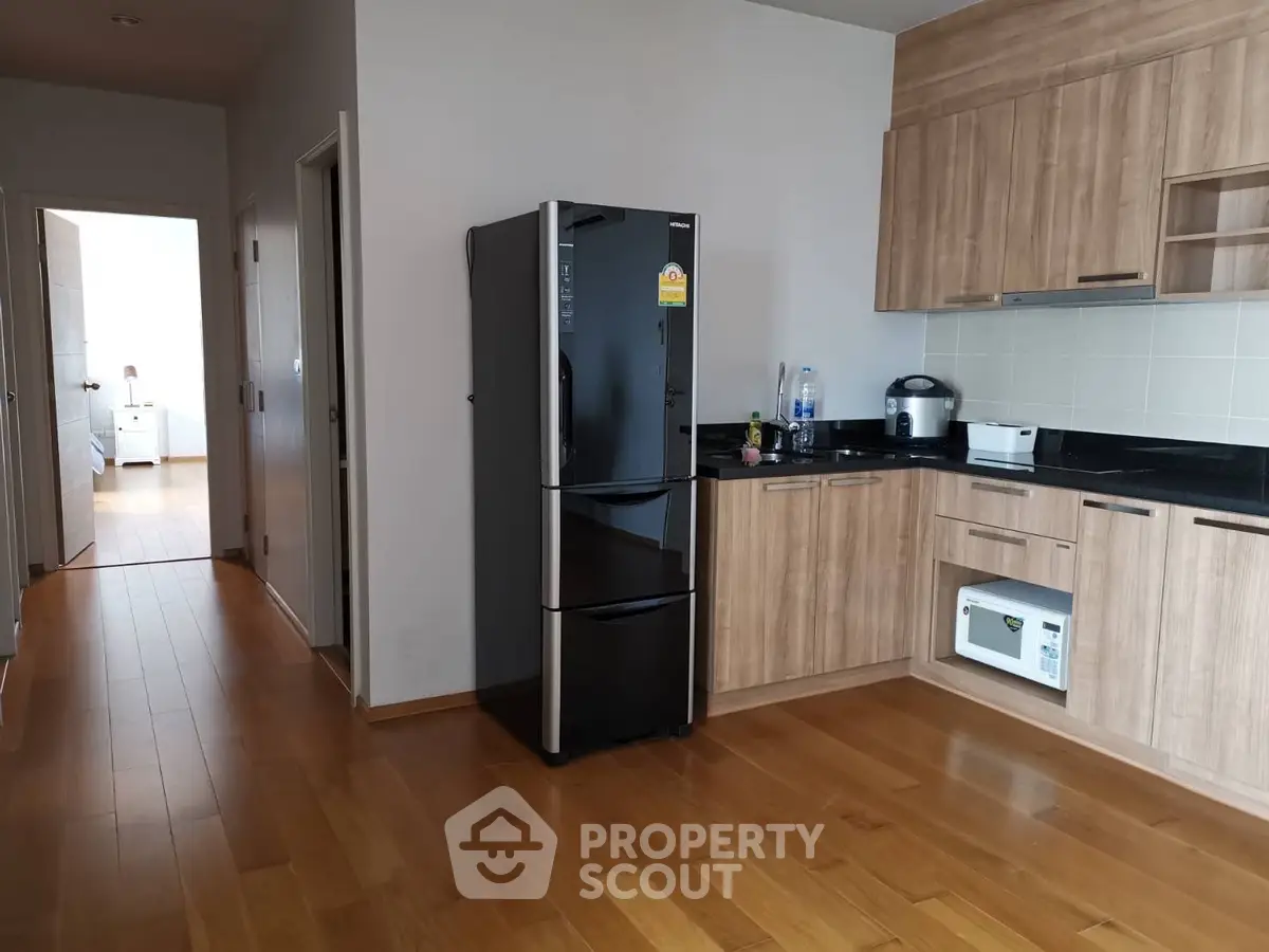 Modern kitchen with wooden cabinets and sleek black fridge in a cozy apartment setting.