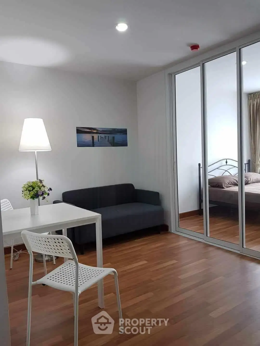Modern apartment interior with cozy living room and stylish bedroom separated by glass doors.