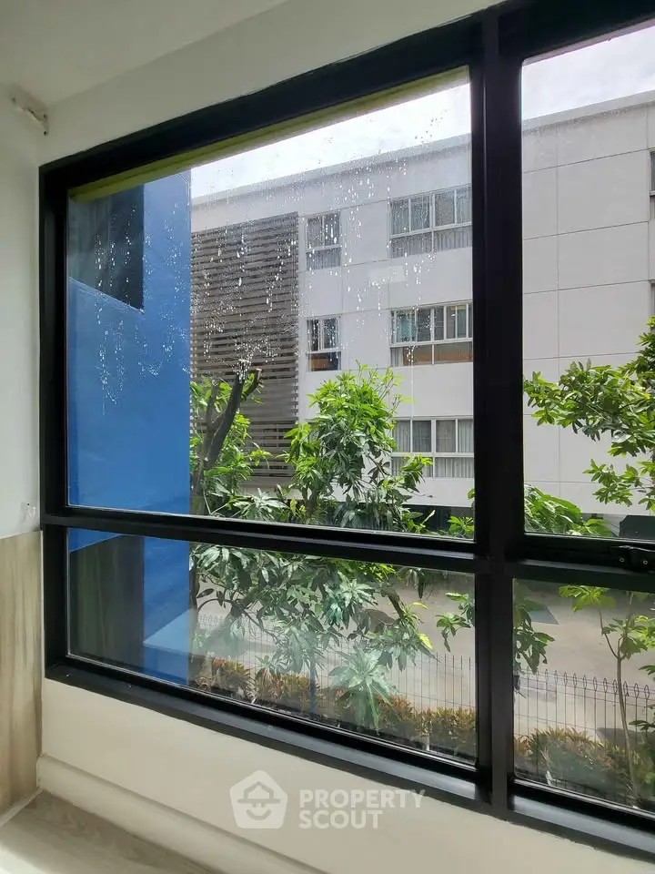 Bright window view showcasing modern building and lush greenery, perfect for urban living.