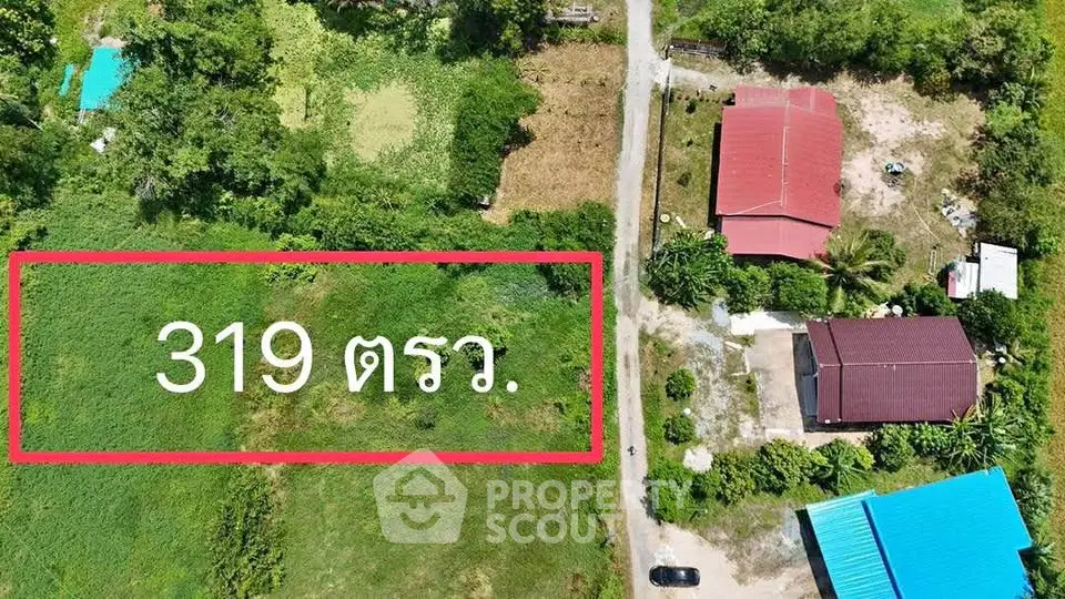 Aerial view of a spacious land plot with buildings and lush greenery, ideal for development.
