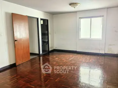 Spacious empty room with wooden flooring and natural light.