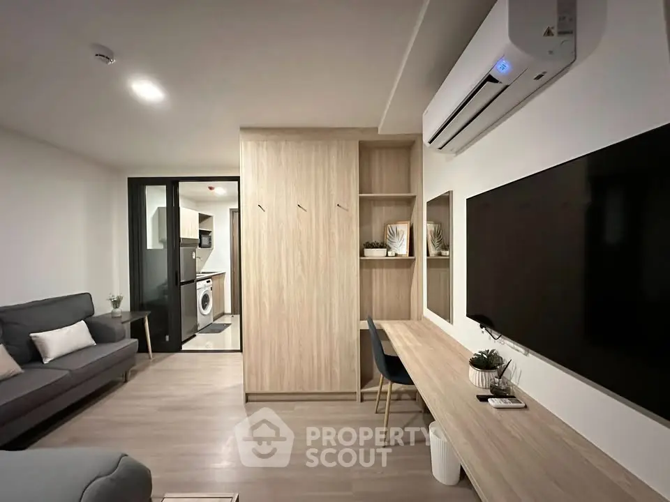 Modern living room with sleek design, built-in storage, and air conditioning, leading to a compact kitchen.