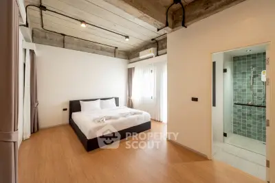 Modern bedroom with ensuite bathroom featuring industrial ceiling and wooden flooring.