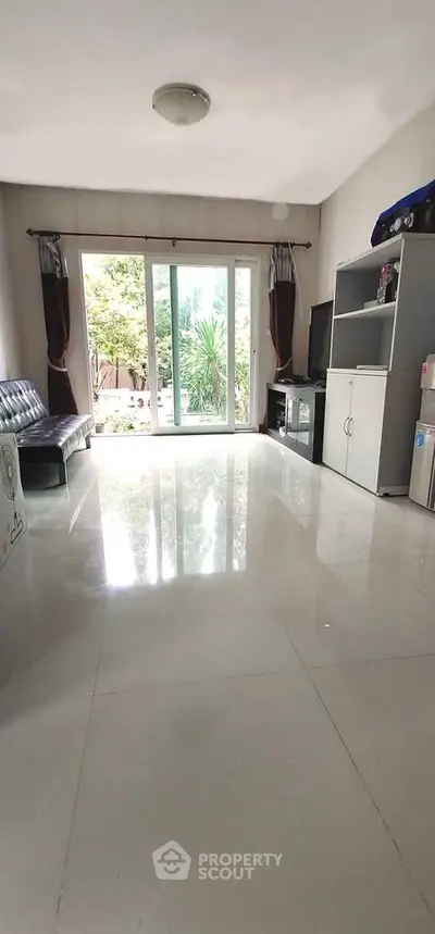 Spacious living room with glossy tiled floors and large sliding glass doors opening to a lush garden view.