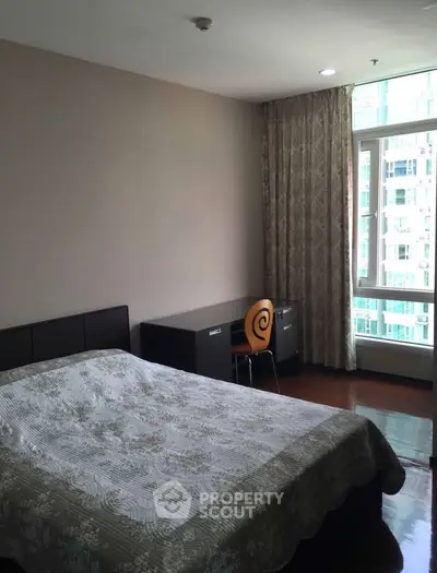 Spacious bedroom with large window and modern furnishings in a high-rise apartment.