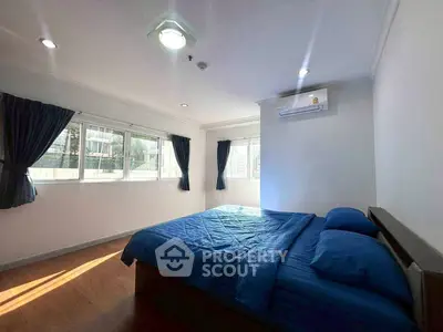 Spacious bedroom with large windows and blue bedding in a modern apartment.