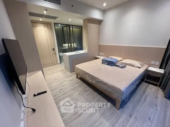 Modern bedroom with sleek design and ensuite bathroom, featuring a mounted TV and stylish flooring.