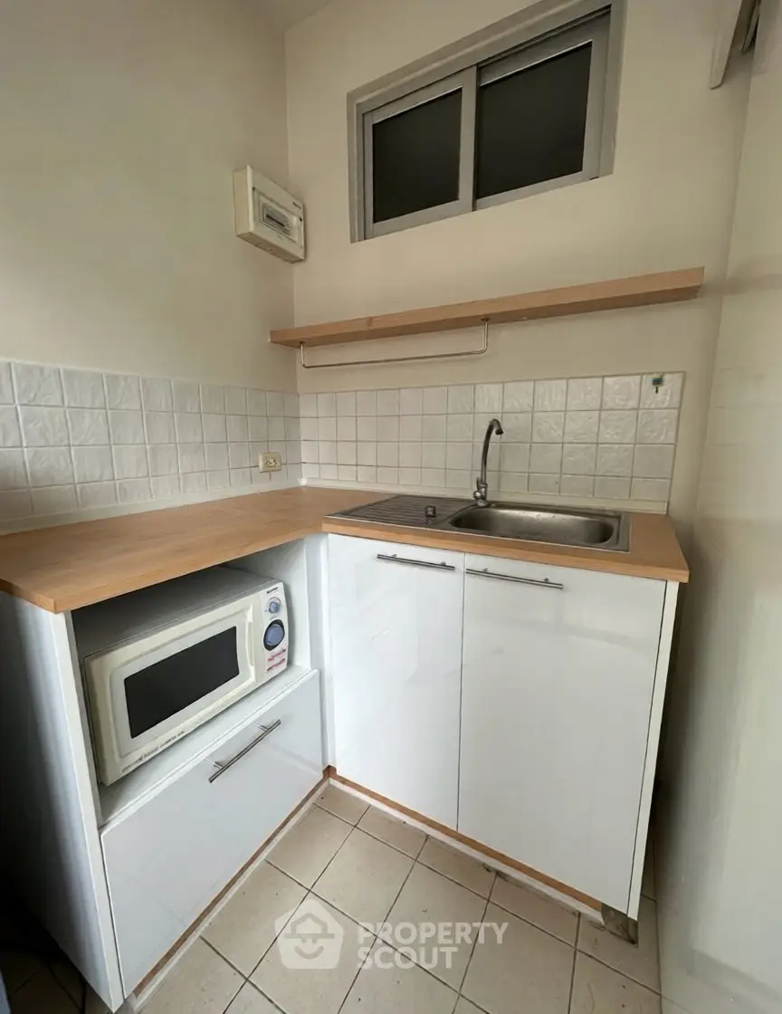 Compact kitchen with modern white cabinets and built-in microwave, featuring a sleek countertop and tiled backsplash.