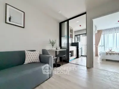 Modern open-plan living room with kitchen and bedroom, featuring sleek furniture and natural light.