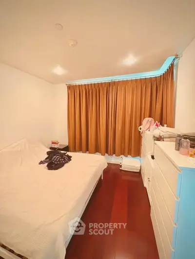 Cozy bedroom with wooden flooring and warm curtains, featuring a comfortable bed and ample storage.