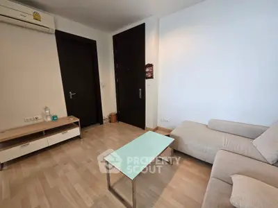 Modern living room with sleek furniture and wooden flooring, featuring a cozy sofa and glass coffee table.