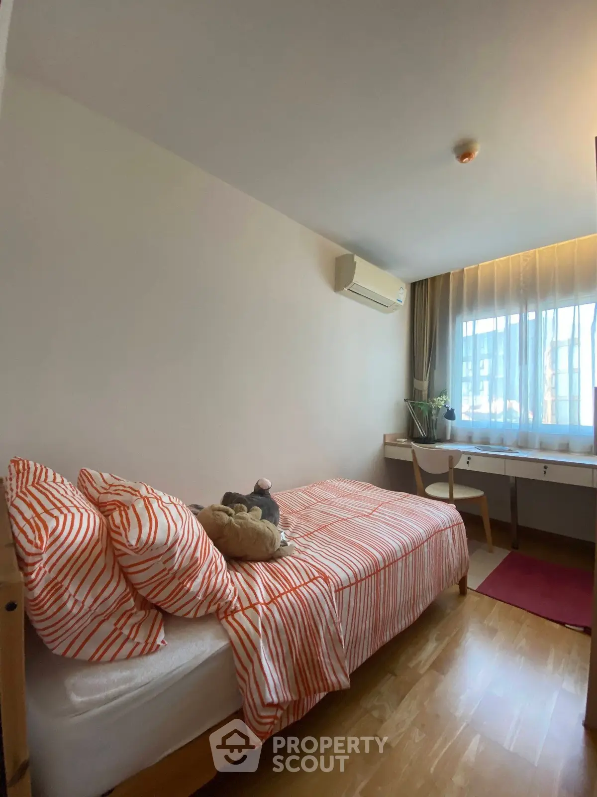 Cozy bedroom with striped bedding, wooden floor, and natural light from large window.