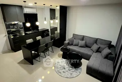 Modern living room with sleek black kitchen, stylish gray sofa, and elegant lighting in open-concept apartment.