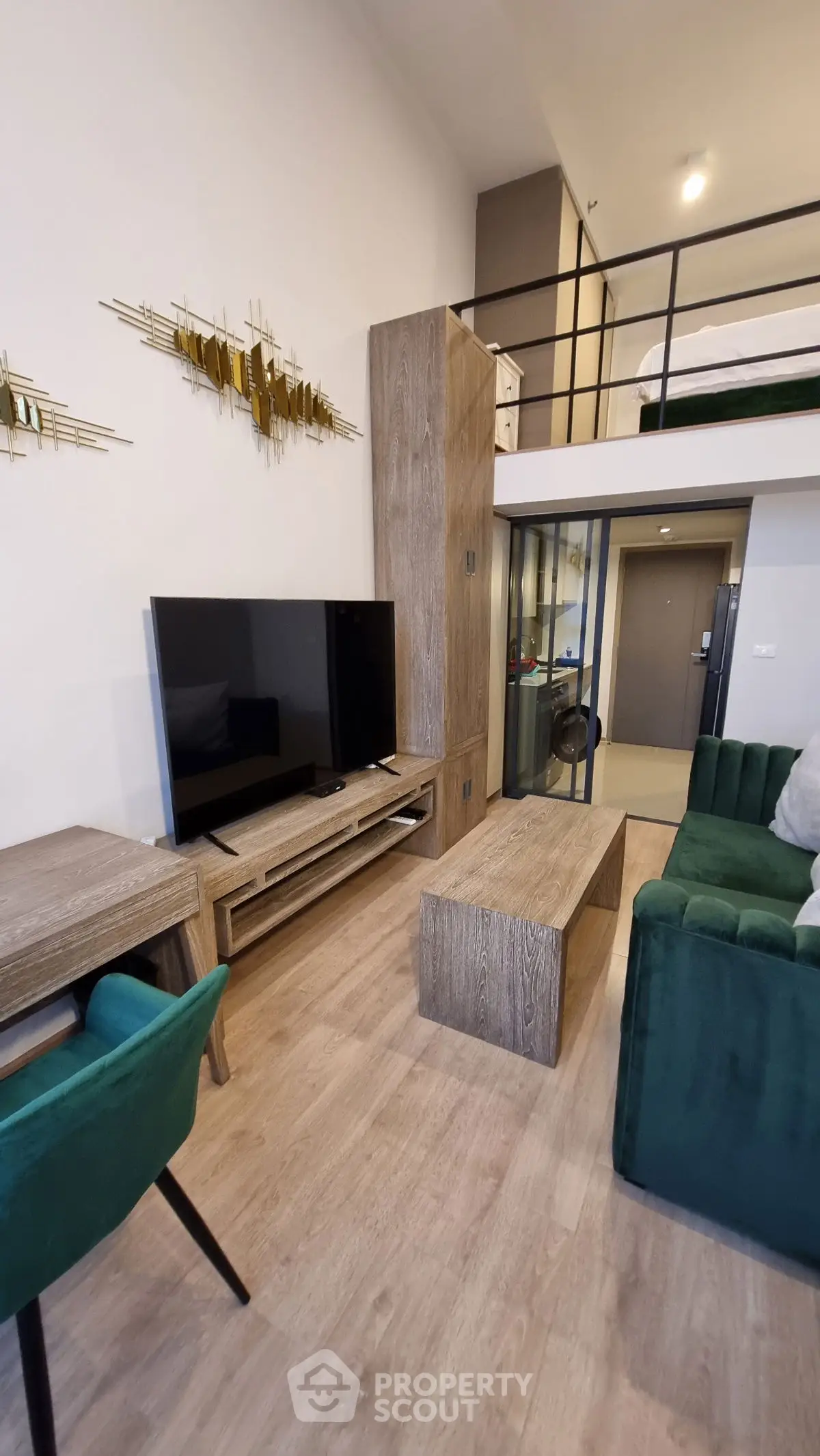 Modern loft-style living room with green velvet sofa and large TV, featuring a mezzanine bedroom.