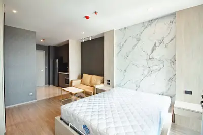 Modern bedroom with stylish decor and open layout, featuring a cozy seating area and elegant marble accent wall.