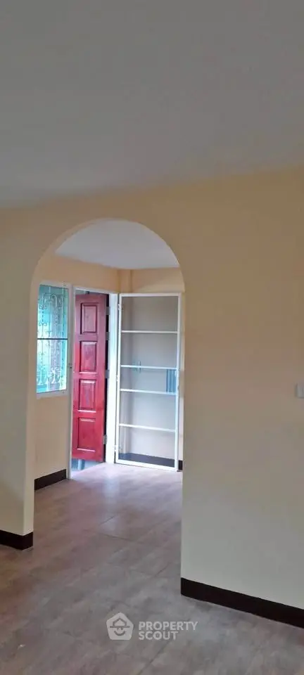 Spacious interior with archway and wooden flooring, featuring a red door and built-in shelving.