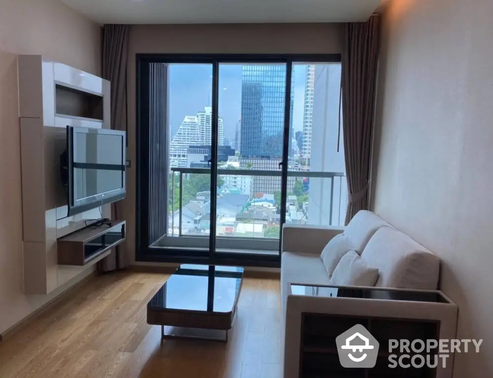 Spacious living room with modern furniture, large windows offering a stunning city view, and hardwood flooring, perfect for urban living.