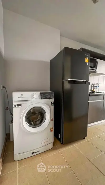 Modern kitchen with washing machine and sleek black fridge in open layout.